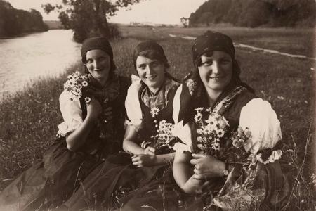 Three young women in German costumes with flowers from the vicinity of Veľká Lomnica in a photo by German professor Alfred Grosz.