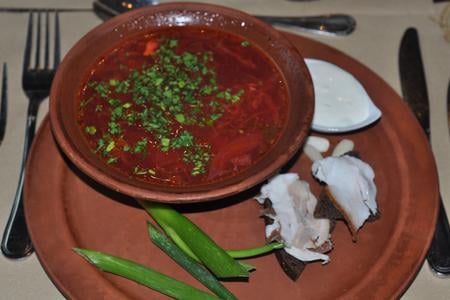 The borsch is attractively presented on simple brown crockery, and accompanied by fresh dark rye bread, ham and garlic.