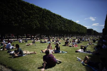 People sit in the sun on a lawn of the Jardin du Luxembourg park in Paris.