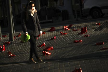 A woman walks among dozens of red painted shoes placed on the ground as a part of an installation against violence against women in Brussels.