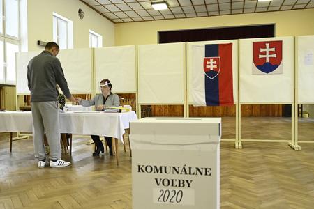 Members of the local election commission register a voter in the list of voters during the by-elections to the local government bodies on October 3, 2020 in the village of Veľká Hradná in the Trenčín Region.