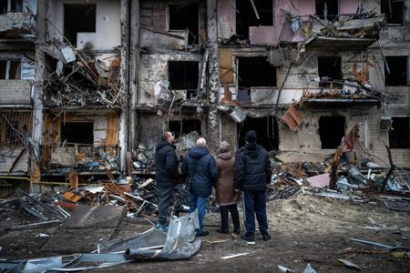 People in Kyiv standing in front of a block of flats destroyed in an air strike. 