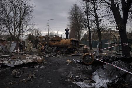 A journalist stands atop a destroyed vehicle after fights between Russian and Ukrainian forces in Bucha, on the outskirts of Kyiv, Ukraine, Wednesday, April 6, 2022.