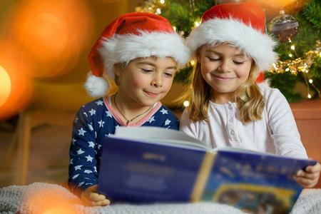 Kids reading book by Christmas tree
