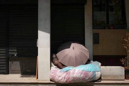 A homeless man is sleeping under an unbrella during a heatwave.