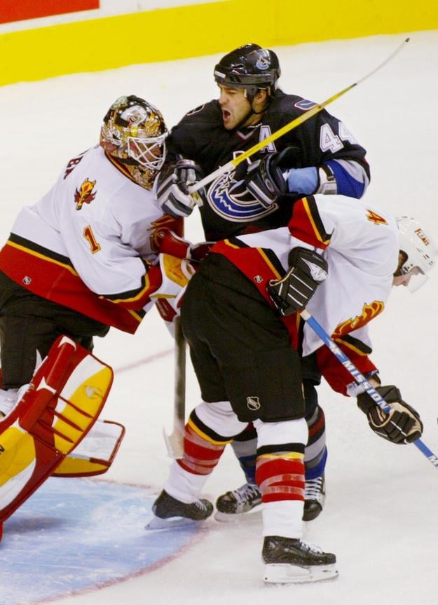 Gólman Calgary Flames Roman Turek odtláča Todda Bertuzziho spred bránky. Vpravo obranca Vancouveru Jordan Leopold. Zo stretnutia NHL Vancouver - Calgary v roku 2003.
