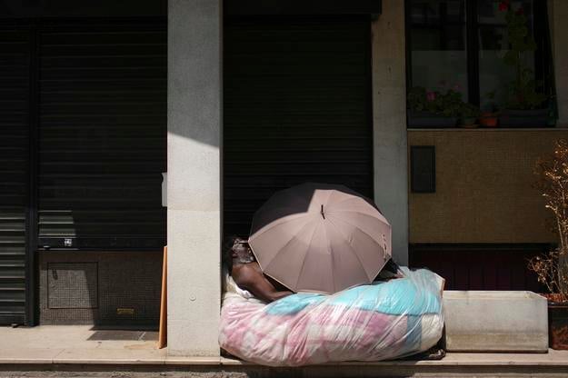 A homeless man is sleeping under an unbrella during a heatwave.