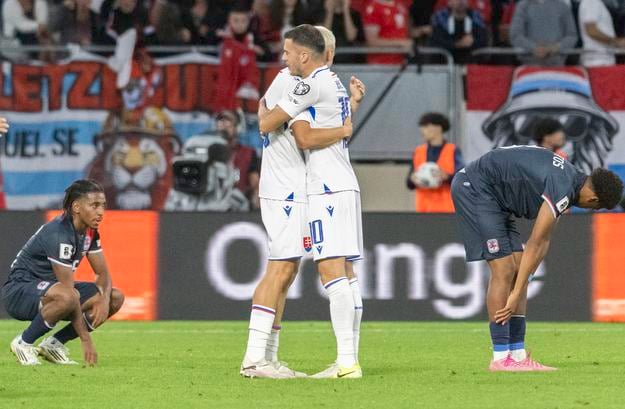 Tomáš Rigo a László Bénes sa objímajú po góle Slovenska, okolo nich smutní hráči Luxemburska.