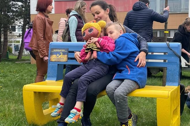 На фото — українська родина сидить на лавці в кольорах українського прапора з нагоди Дня Землі у місті Prievidza, квітень 2022 року.