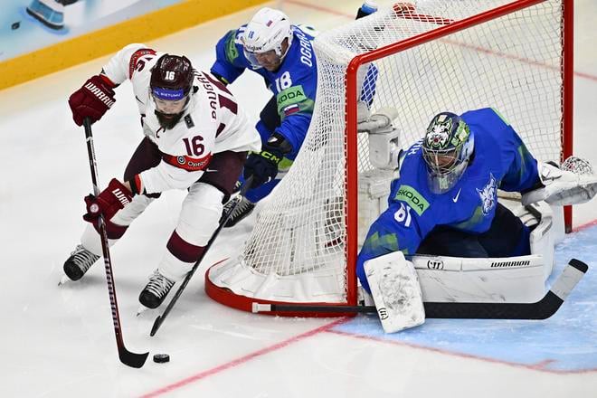 Lotyšský hráč Kaspars Daugavins(vľavo) v akcii pred Slovincom Kenom Ograjensekom (uprostred) a slovinským brankárom  Lukasom Horakom (vpravo) v zápase A-skupiny Slovinsko - Lotyšsko na MS 2025 v hokeji vo švédskom Štokholme.