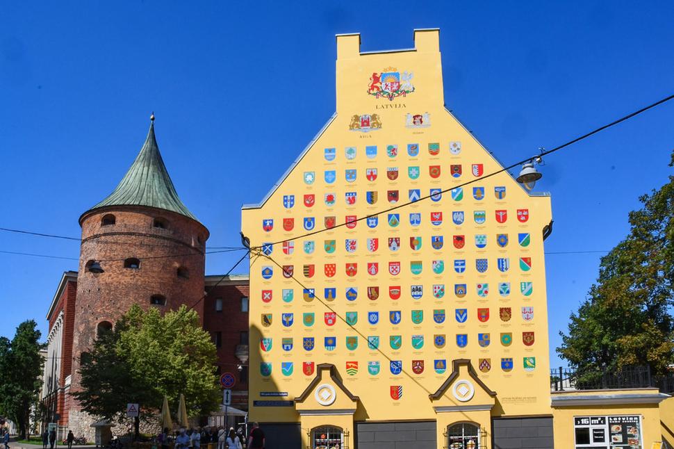 Iný pohľad na Prašnú vežu. Na fasáde žltej budovy sú symboly všetkých lotyšských miest. Je to bočná stena Švédskych kasární, ku ktorým smerujeme.