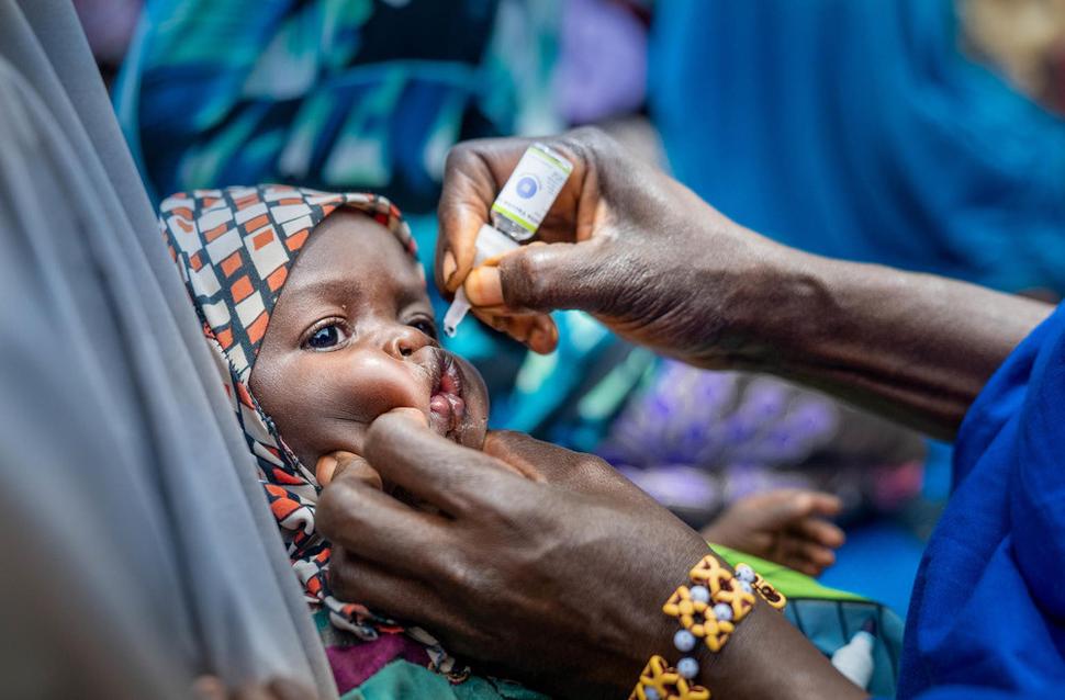 Dobrovoľníčka v Nigérii očkuje bábätko proti obrne počas slávnosti udeľovania mien. Terénni pracovníci často na svoju osvetovú činnosť využívajú rôzne komunitné a rodinné stretnutia, a pri tejto príležitosti sa deti očkujú proti nákazlivým ochoreniam.