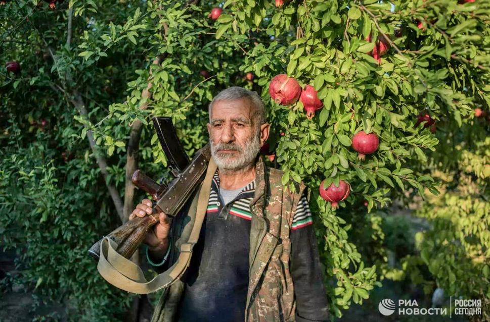 Obyvateľ dediny Uchtasar Anushavan stojí v záhrade pod stromom s granátovými jablkami neďaleko svojho domu. V ruke drží starý samopal Kalašnikov, ktorý mu zostal z Prvej Karabašskej vojny.