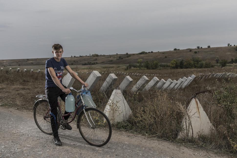 Ukrajina, 2018: Dima Mikhalyov, 15, nesie vodu v kanistroch na svojom bicykli pozdĺž poľa s protitankovými bariérami v blízkosti Bakhmutky v regióne Doneck.