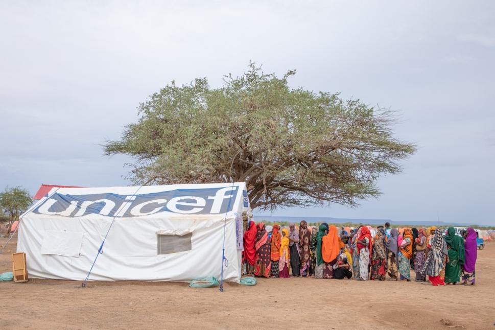 Ženy a deti stoja v rade na pomoc v tábore pre vnútorne vysídlené osoby Higlo, kde tímy pracovníkov podporované UNICEFom distribujú život zachraňujúci humanitárny material.