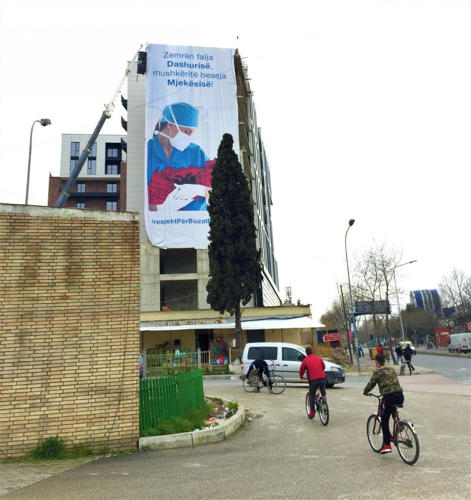 Street scene in Tirana. Text on transparent: “Give your heart to love, and for your lungs trust Medicine.”