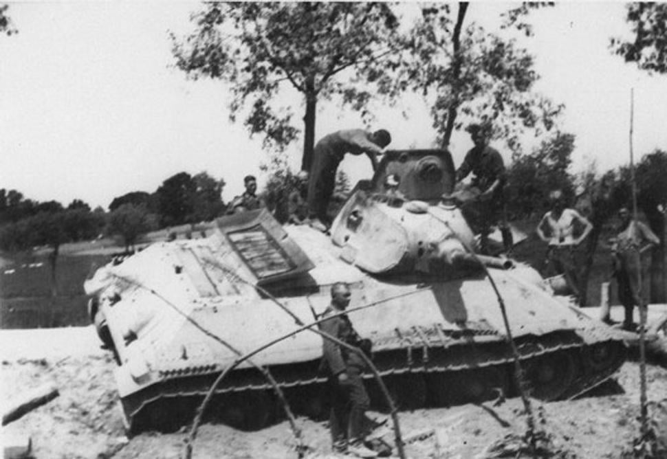 Nemeckí vojaci si prezerajú zničený sovietsky tank T-34 s pôvodným delom L-11, a v tej dobe ešte pôvodnou, malou tankovou vežou. Pod Dubnom, jún 1941.