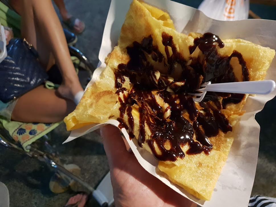 Hotová banánová palacinka s čokoládovou polevou a na papierovej tácke pokrájaná na malé štvorčeky.