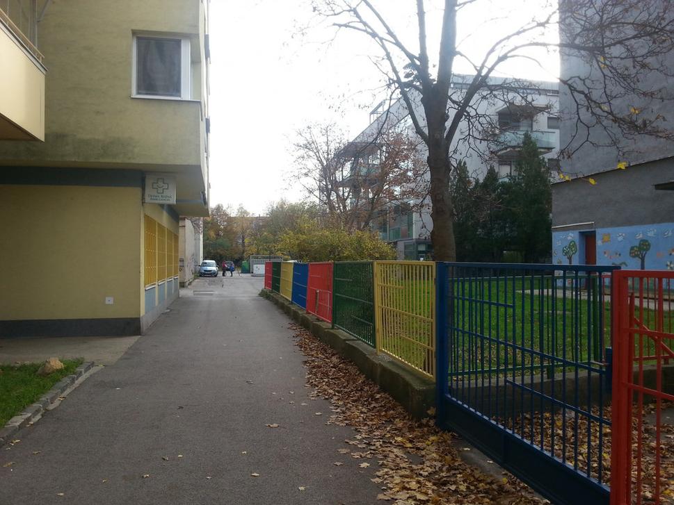 Vľavo bývalá centrála Smeru, dnes nadstavba s bytmi elegantne prechádzajúcimi ponad chodník. Vpravo, kde končí plot začína bytový dom citlivo včlenený do ihriska základnej školy. 